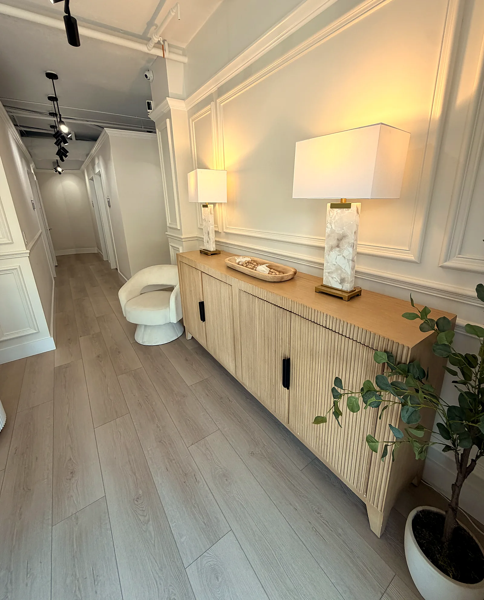 Hallway with a fluted oak sideboard, alabaster lamps, and a potted plant.