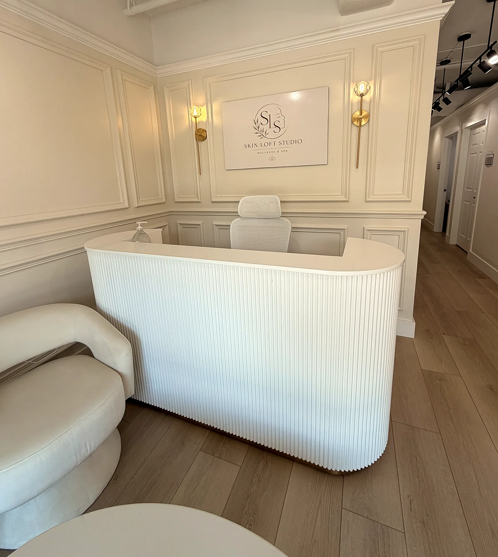 Reception at Skin Loft Studio: a fluted white desk, brass sconces, and the framed studio logo.
