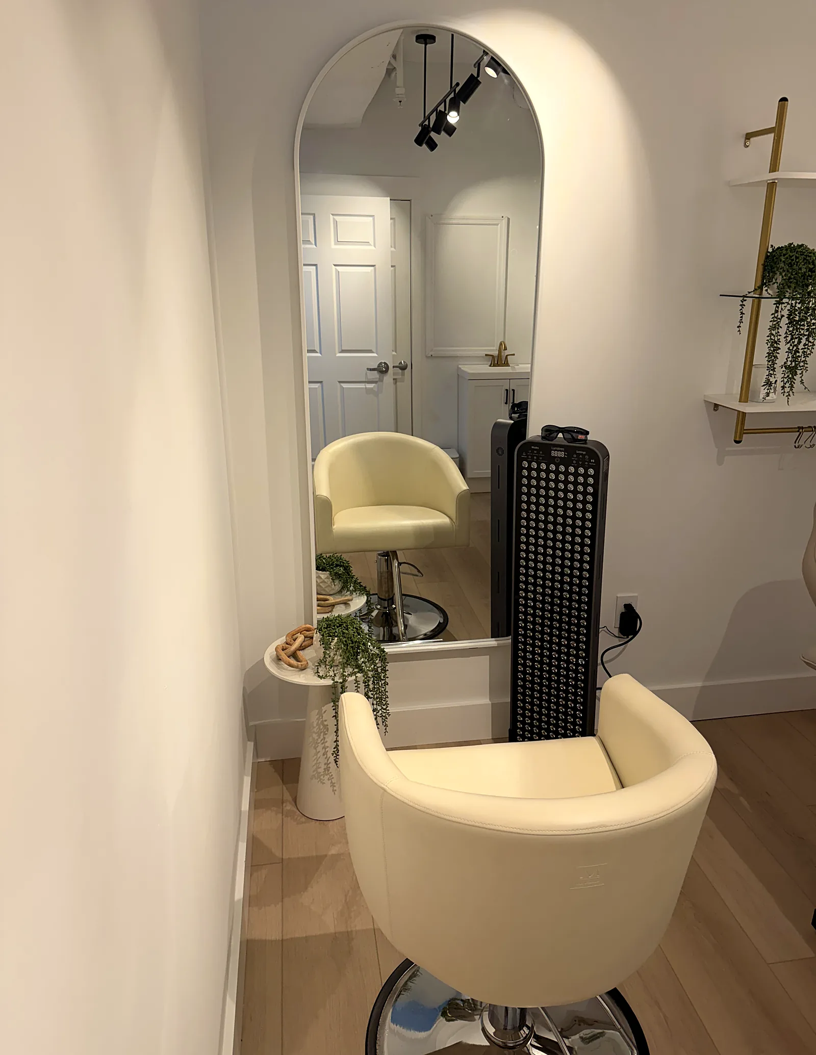 A red light therapy panel beside an arched mirror and a cream chair.